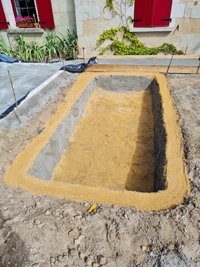 Construction d'un bassin en bâche, le trou a été creusé et du sable a été déposé au fond et sur les margelles.